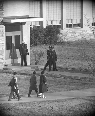 Three police officers stand at the entrance to Stratford Jr. High School as the four black students enrolled in the previously all-white school arrive for classes in Arlington, Va., on Feb. 2, 1959. One of the officers records the scene with a movie camera. Approaching the entrance are, left to right, Lance Newman, 13, Ronald Deskins, 12, Michael Jones, 12, and Gloria Thompson, 12. (AP Photo)