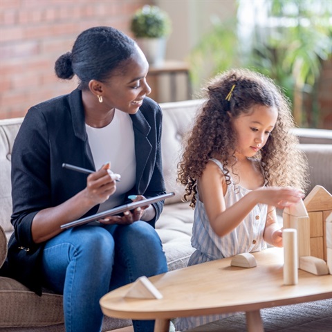 Child building structure from wood blocks while adults speaks to her