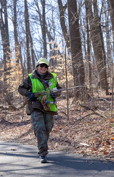 Smiling volunteer wearing a safety vest carries branches and a lopper