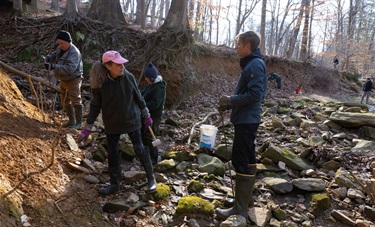 Seven volunteers and eroding streambank. Volunteers hold rebar, mallets, and cut branches