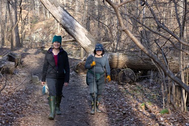 Two smiling volunteers walk along a path next to Gulf Branch, holding rebar and a pair of gloves