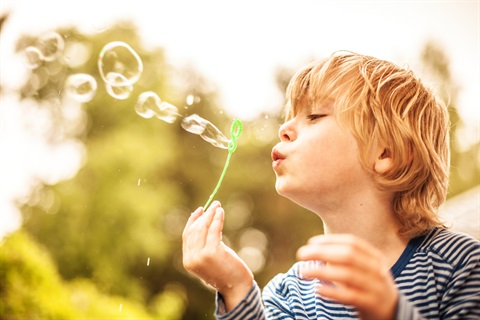 young boy blowing bubbles in a grassy field