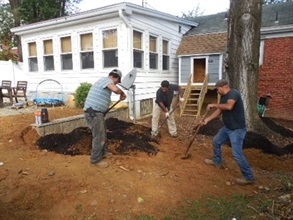 Three men digging and planting mulch in front of a house